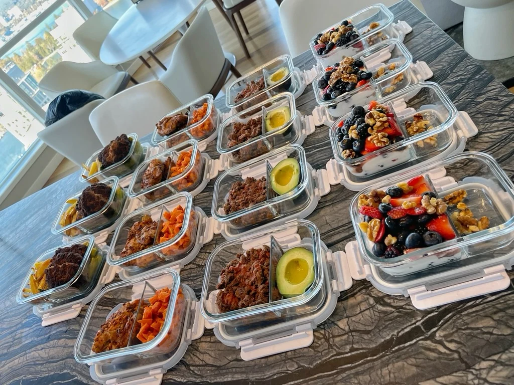Prepared meals with meat, vegetables, avocado, yogurt, berries, and nuts in glass containers